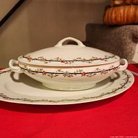 Covered vegetable bowl with lid on matching platter showing floral border