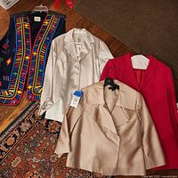 Four women’s outerwear pieces laid out on floor: colourful vest, silver blazer with tags, beige jacket, red blazer