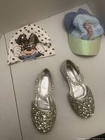 Front view of Minnie Mouse hat, Frozen Elsa cap, and silver glitter shoes