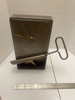Front view of rectangular metal clock with stand piece, ruler for scale