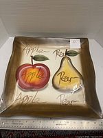 Front view of square platter showing apple and pear design with ruler for scale