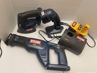 Group view of Ryobi reciprocating saw, corner sander, flashlight, battery, charger