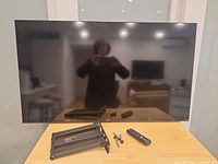 Front view of TV with remote, wall mount and screws on table