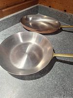 Top view of both pans showing stainless interiors and brass handles