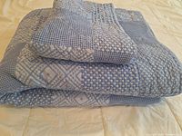 Folded chambray blue quilted bedspread with pillow sham on top