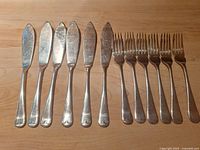 Six fish knives and five forks aligned on wood surface