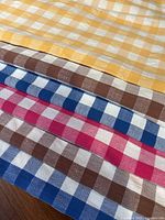 Stacked view of yellow, brown, blue, red gingham tablecloths showing check pattern and fabric texture