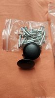 Bag of metal screws and two black round knobs on orange cloth