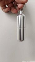 hand holding single aluminum pill container showing size and key ring