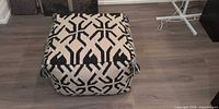 Front angled view of square black and white patterned pouf with tassels