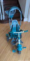 Front view showing teal-aqua trike, canopy, footrest, safety bar and wheels