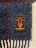 Close-up of maker tag and fringe on blue plaid cashmere scarf