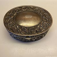 Top view of oval silver-plated box showing embossed foliage design and central cartouche