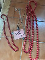 All five necklaces laid out showing red bead strands and various pendant necklaces
