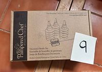 Front of boxed Pampered Chef Decorator Bottle Set showing illustration of three bottles and cleaning brush