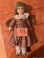 Front view of porcelain doll in plaid dress lying on tiled floor