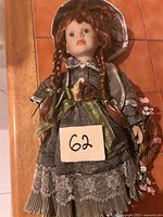 Front view of porcelain doll with green dress, bonnet and basket, stand not visible