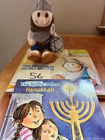 Plush Maccabee doll sitting on two books
