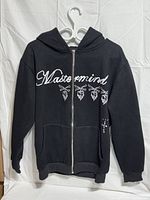 Front view of black hoodie showing Mastermind script, skull graphics, full zipper, kangaroo pocket