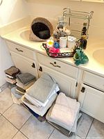 Countertop view with towels, wicker wastebasket, metal shelf rack, seashell jar, decorative tray and ceramic frog