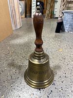 Full view of brass bell showing wood handle and "CAPTAIN" engraving