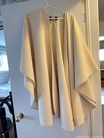 Full view of cream open-front cape hanging on hanger