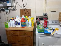 Overall lot on cabinet and dryer showing boxed Bissell vacuum, cleaning chemicals and accessories