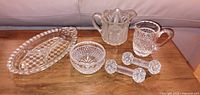 All six pressed glass pieces on wooden surface: tray, two creamers, sugar bowl, two stirrer rests