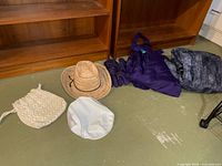 Group shot of all items on floor: straw hat, visor, macramé purse, purple jacket, grey fleece item