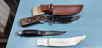Overall view: two knives with respective sheaths laid on blue surface