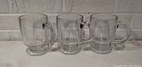 Front view of three matching clear footed glass mugs