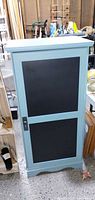 Front view of teal cabinet showing black chalkboard door panels and latch