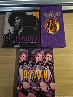 All three items laid out: Hendrix illustrated book, Hendrix purple CD box, Dylan CD box
