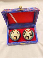 Pair of Baoding balls inside open blue brocade box, showing mask design and red interior