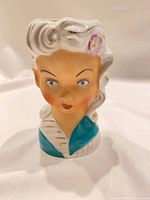 Front view of ceramic lady head vase showing facial features, flower accent, color details
