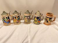 Front view of five steins showing decorative scenes and lids