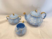 Front view of teapot, sugar bowl, creamer showing colour, pattern and gold trim