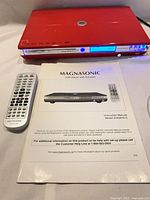 Front view of red Magnasonic DVD816-C player with remote and manual
