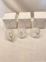 Three clear iridescent glass ornaments in front of three white boxes