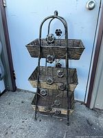 front view showing full stand with three wicker baskets and decorative metal flowers