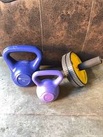 Blue and purple kettlebells next to yellow ab roller