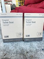 Front view of two sealed boxes labeled Elongated Toilet Seat