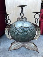 Front view of fish-shaped metal candelabra showing three arms and patina