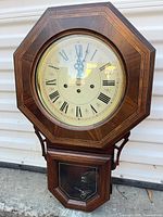 Front view of Howard Miller octagonal wall clock showing dial and lower door