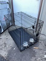 Overall view of black wire folding dog crate with tray and bowls