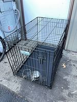 Overall view of black wire dog crate with bowls and tray in place