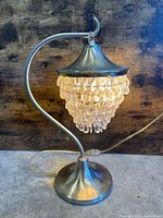 Full view of illuminated brushed nickel table lamp showing curved stem, base and crystal drops