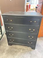 Front view of black 4-drawer dresser showing overall style, hardware and finish wear