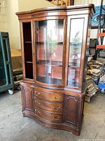 Front view of tall wooden curio cabinet showing curved glass door, side glass panels, and base drawers