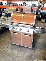 Front view of Weber Genesis copper grill showing hood, control panel with three knobs, cabinet base